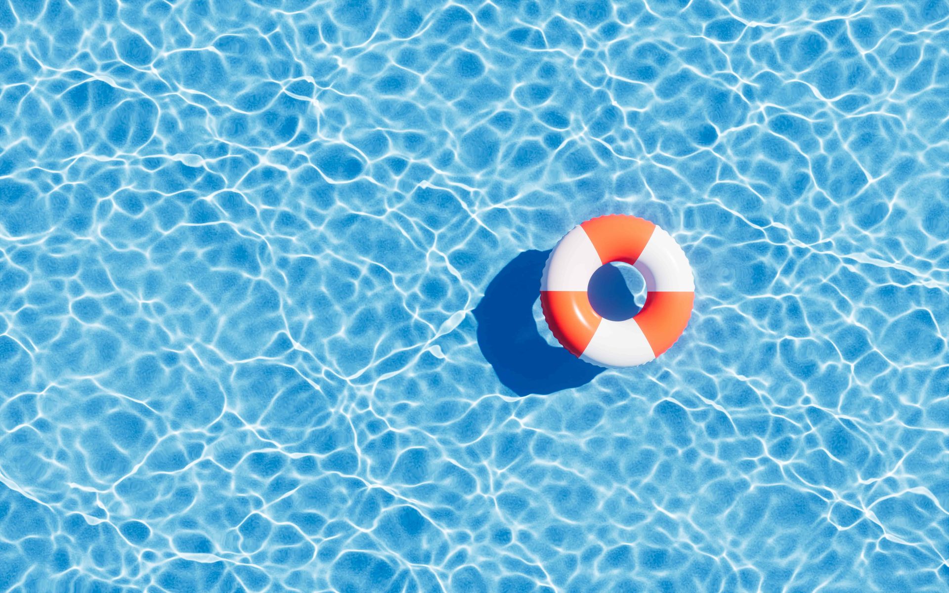 Orange and white life ring floating in a sparkling blue swimming pool, overhead view.