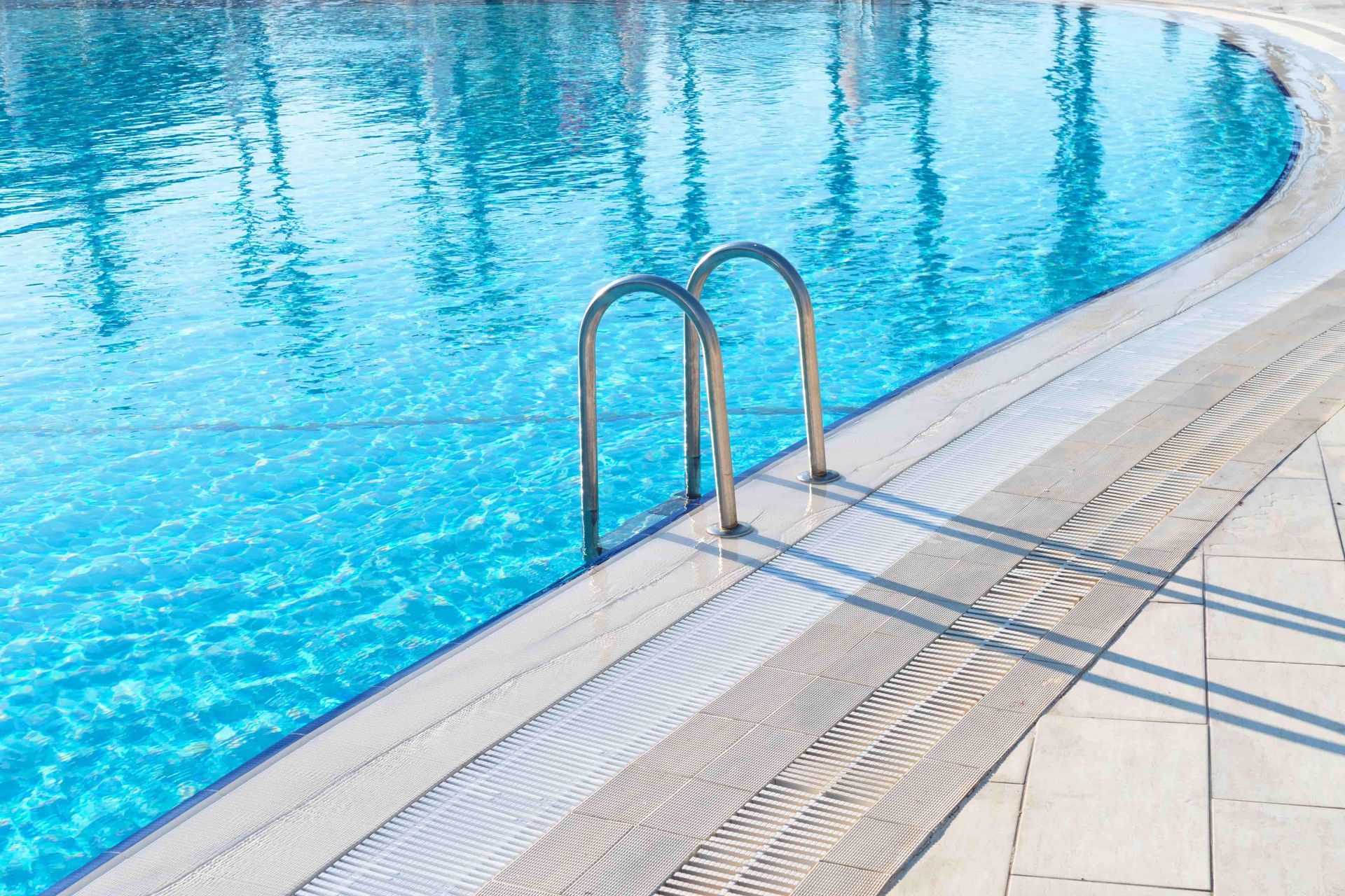 Swimming pool with blue water, metal ladder, and light-colored deck.