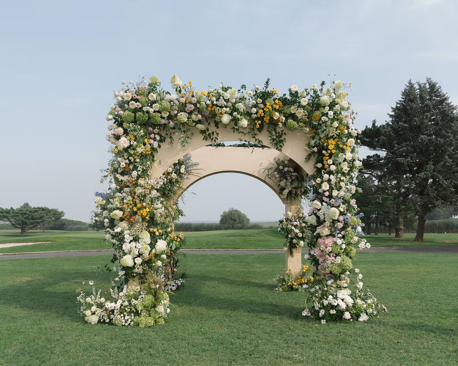 Flower-covered archway on a grassy lawn with trees in the background