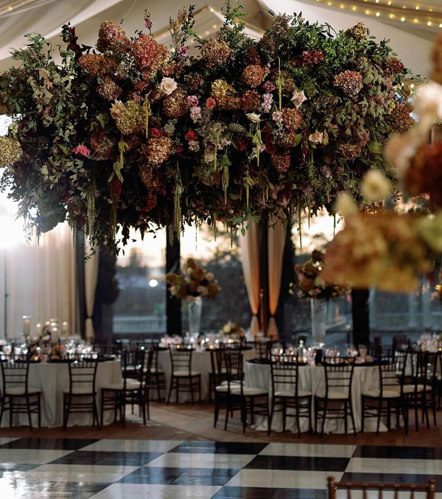 Elegant banquet hall with a large floral ceiling installation, round tables, and checkered dance floor