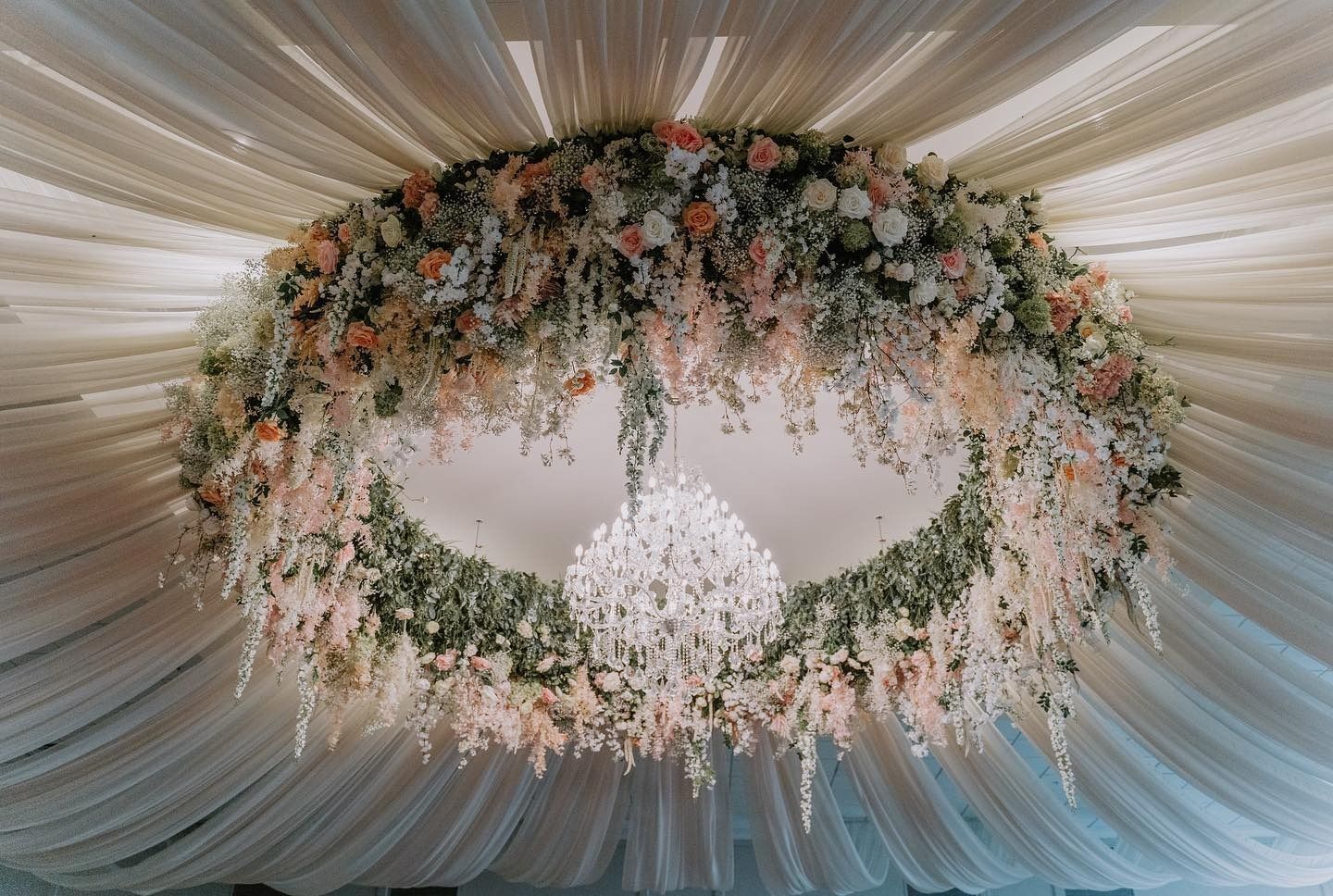 Floral chandelier centerpiece under a draped white ceiling at an elegant event venue