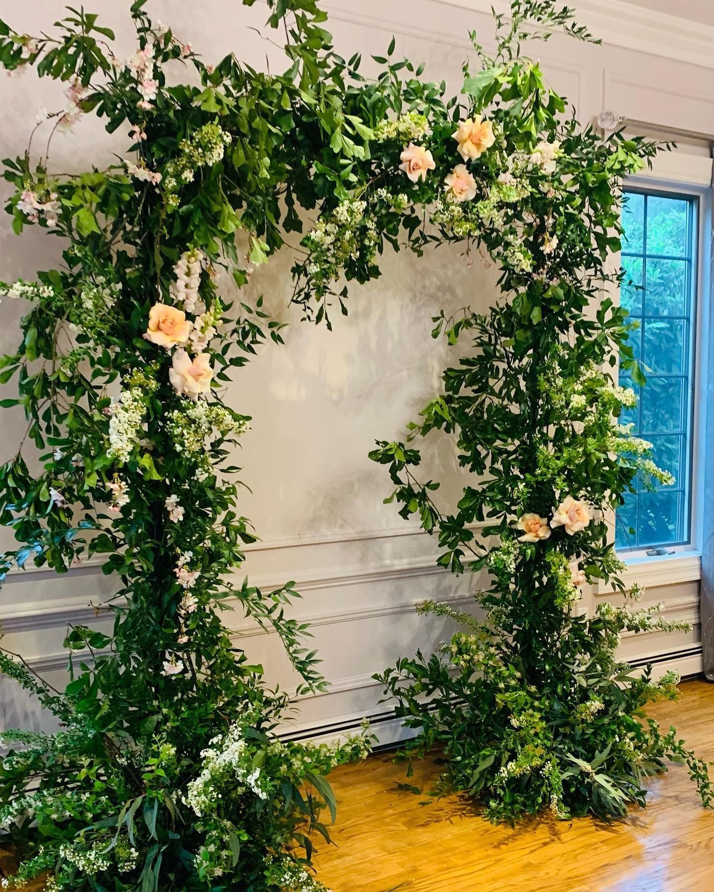 Floral arch of greenery and pale pink roses against a white wall near a window