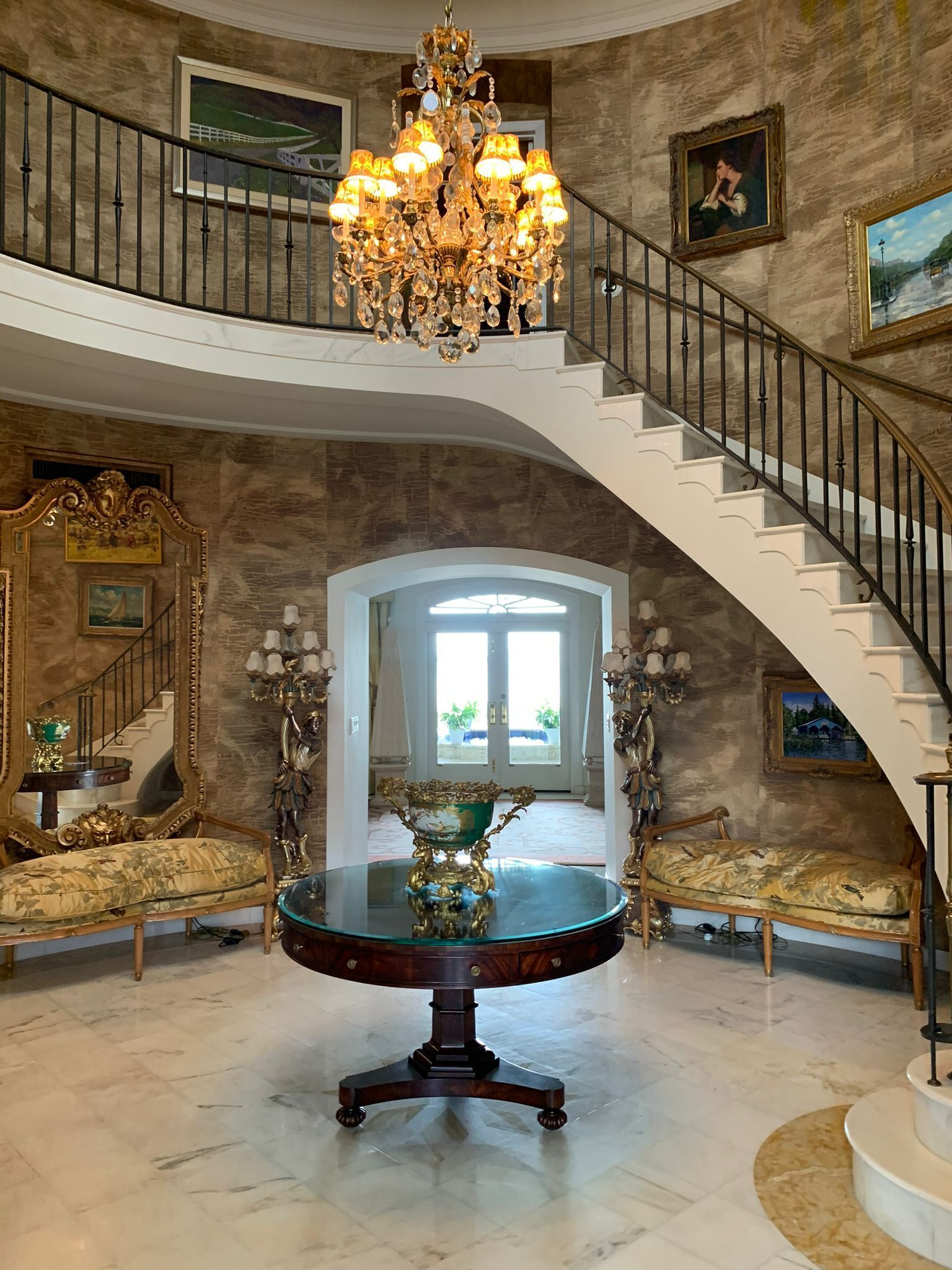 There is a staircase in the middle of the room with a chandelier hanging from the ceiling.