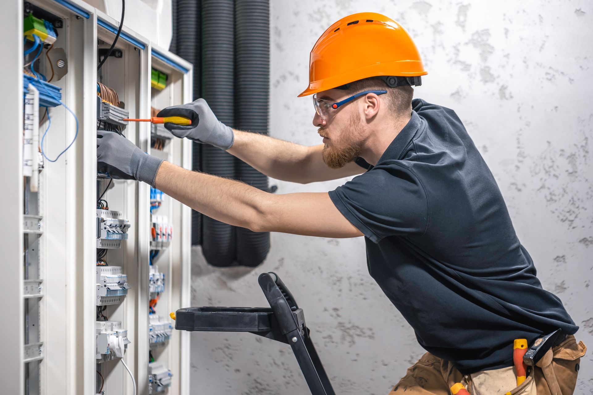 A man wearing a hard hat and safety glasses is working on an electrical box.