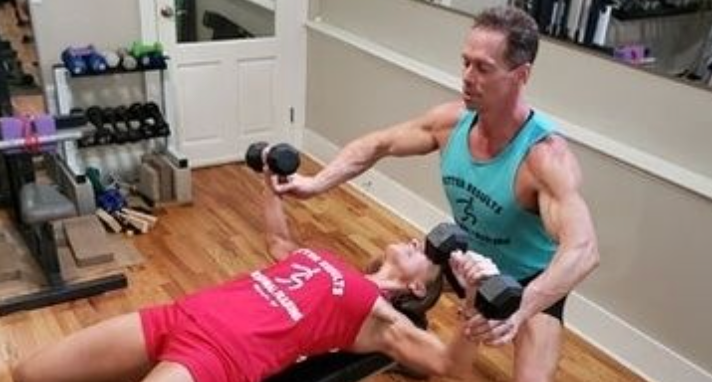 A man is helping a woman lift dumbbells on a bench.
