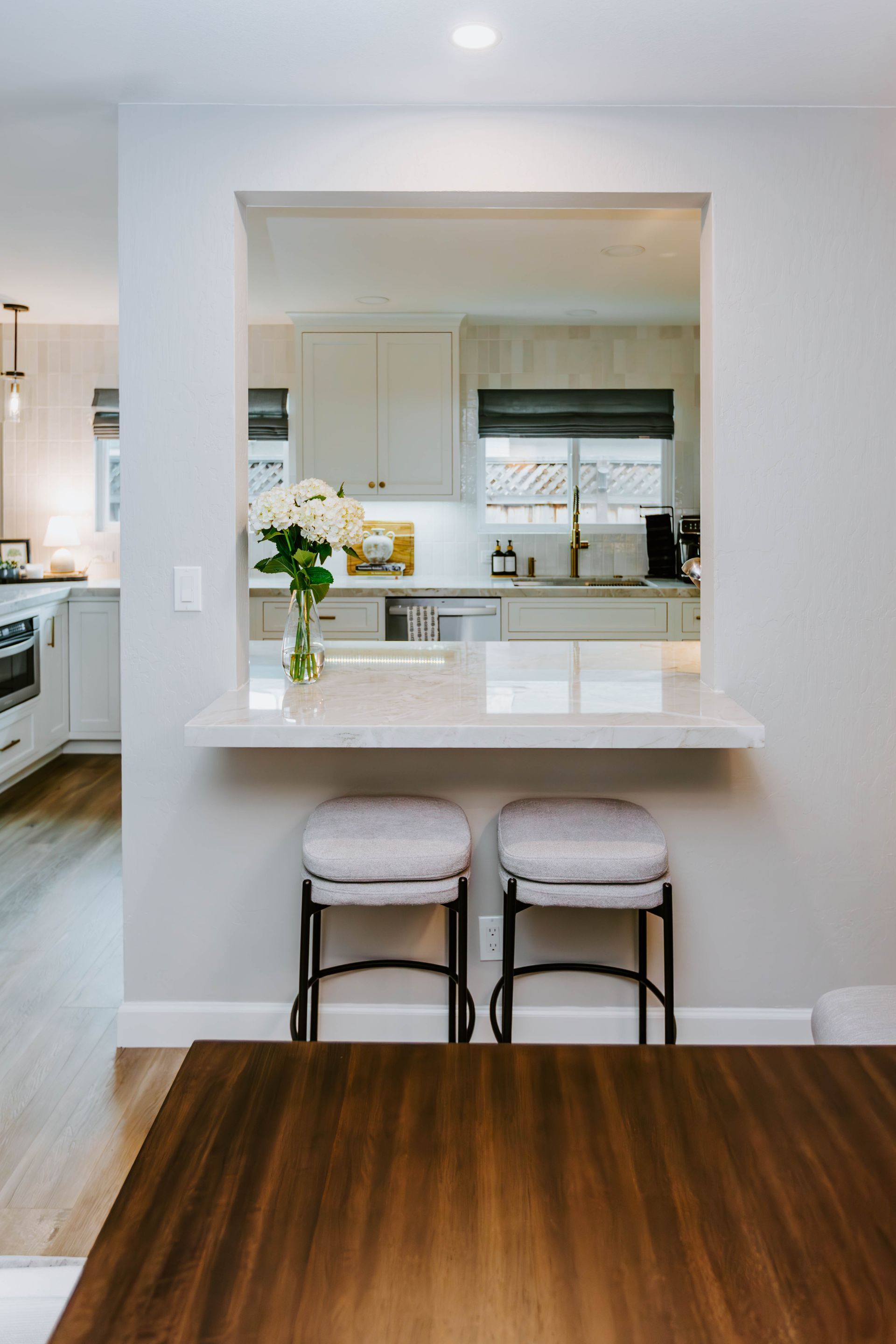Kitchen pass-through with countertop and stools; view of kitchen with white cabinets.