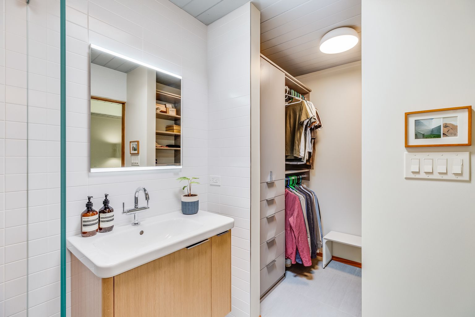 A bathroom with a sink , mirror and walk in closet.