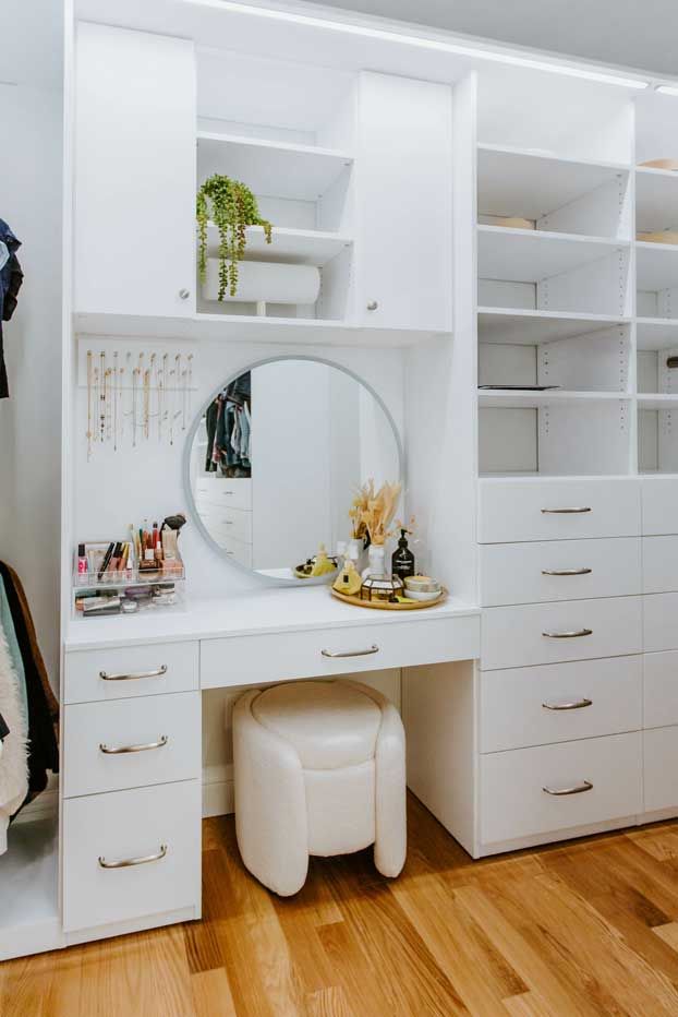 There is a vanity with a round mirror and a stool in the closet.