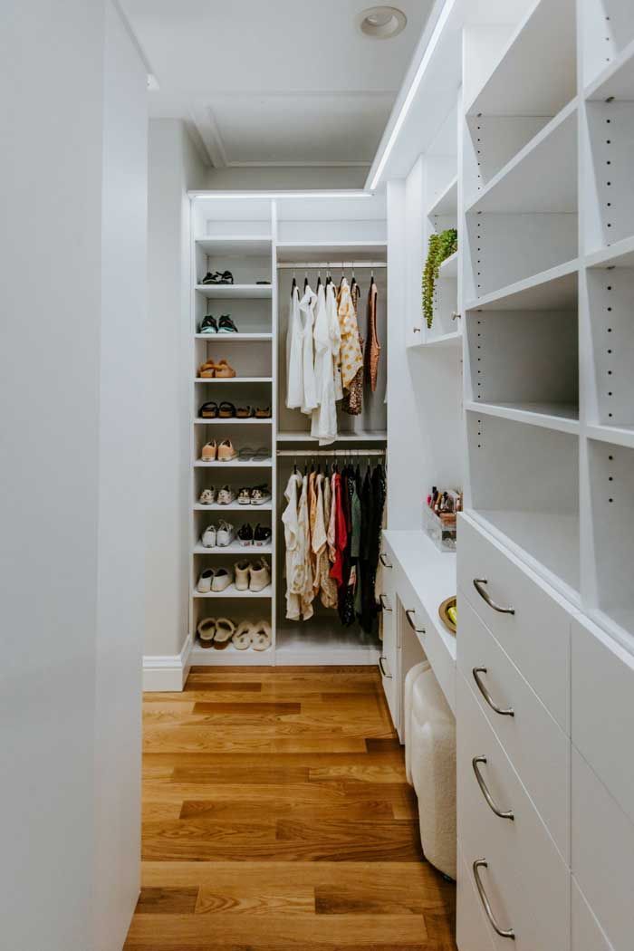 A walk in closet with wooden floors and white shelves filled with clothes and shoes.