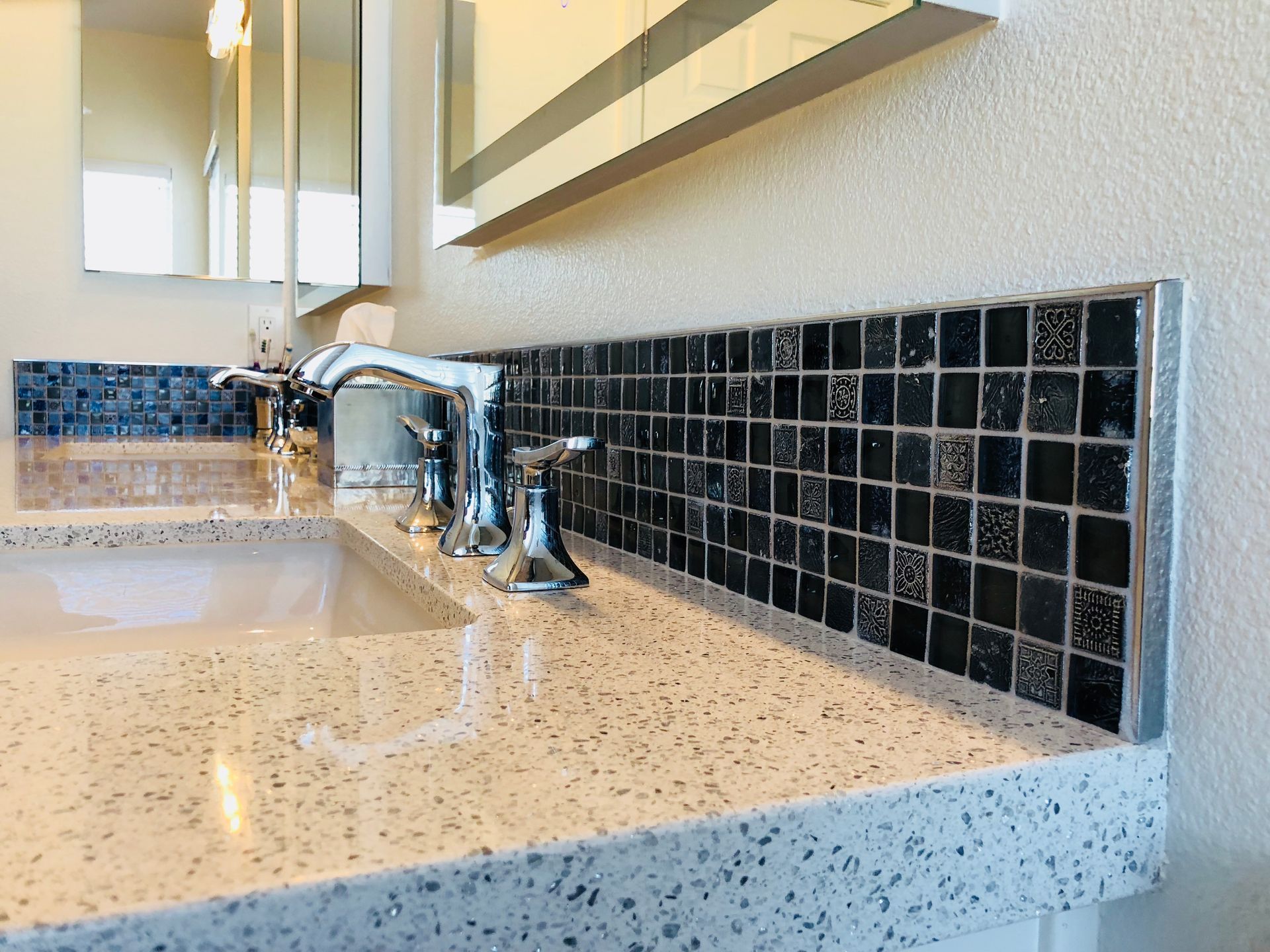 A bathroom sink with a black tile backsplash and a mirror.