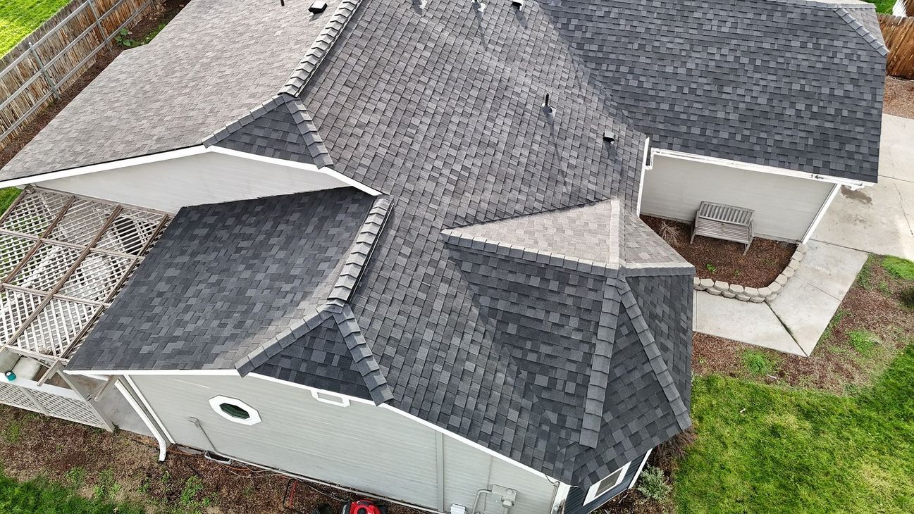 Overhead view of a house with a complex shingled roof, light gray siding, and a small yard.