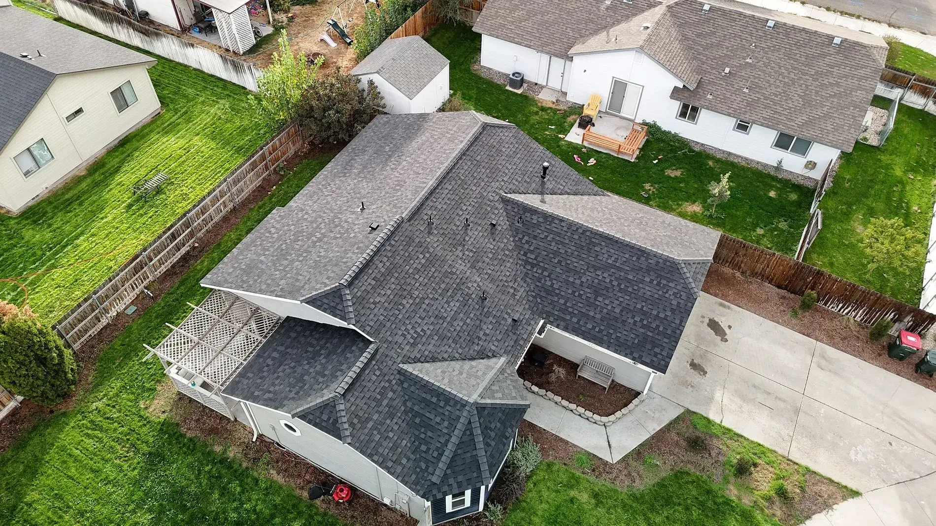 Aerial view of a gray-roofed house with a driveway, surrounded by green grass and neighboring houses.