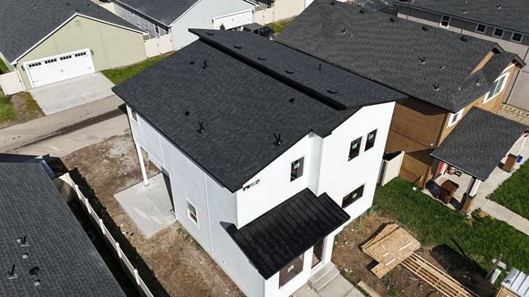 Aerial view of a white two-story house with black roof and accents, adjacent to other houses.