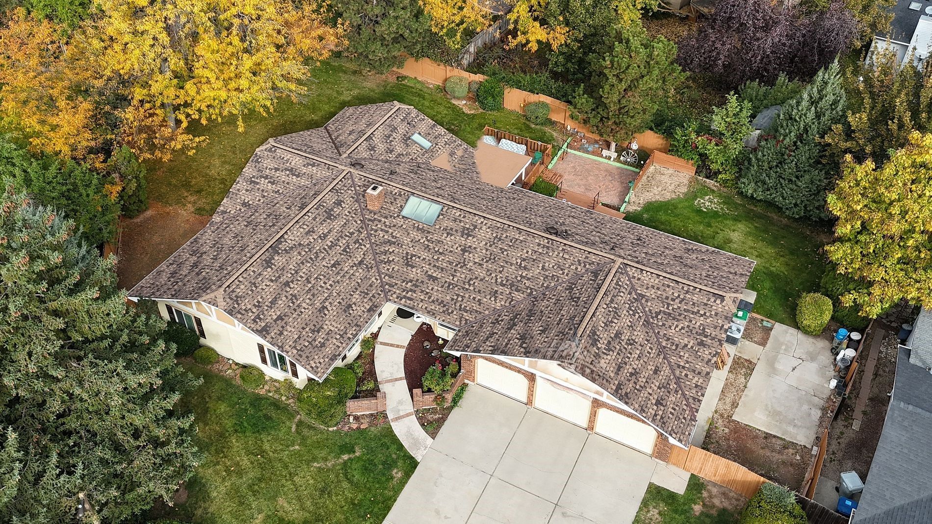 Overhead view of a house with a brown roof and surrounding trees with colorful foliage.