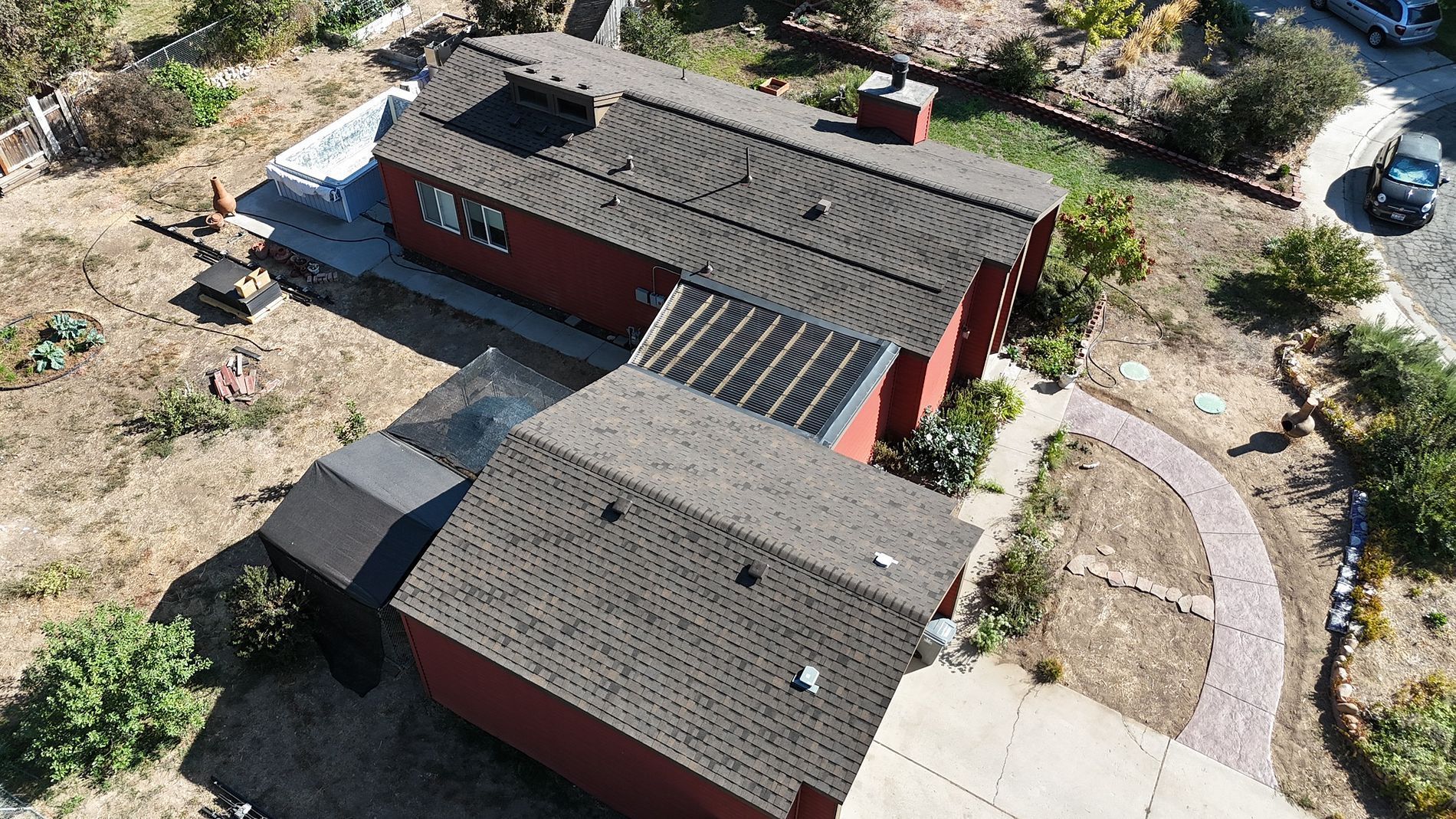 Aerial view of a red house with dark gray roof, surrounded by dry grass and some greenery.