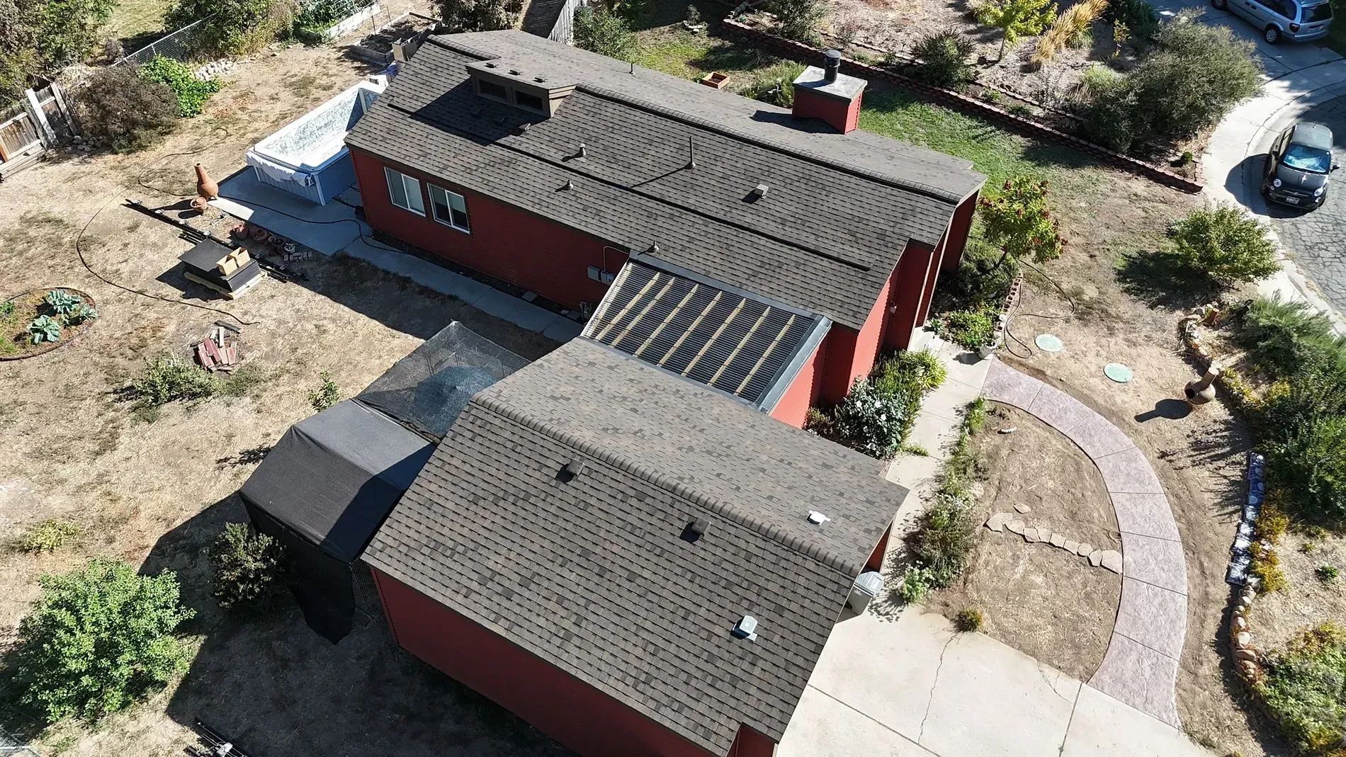 Aerial view of a red house with dark gray roofs, a patio, and a curved brick pathway.