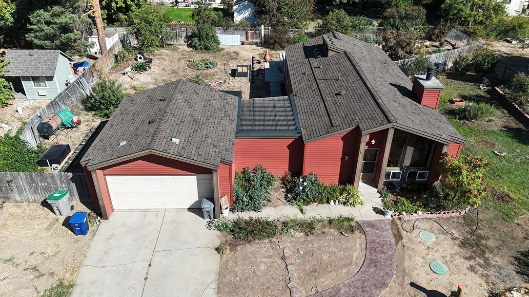 Red house with a garage and a dark roof. Concrete driveway in front.
