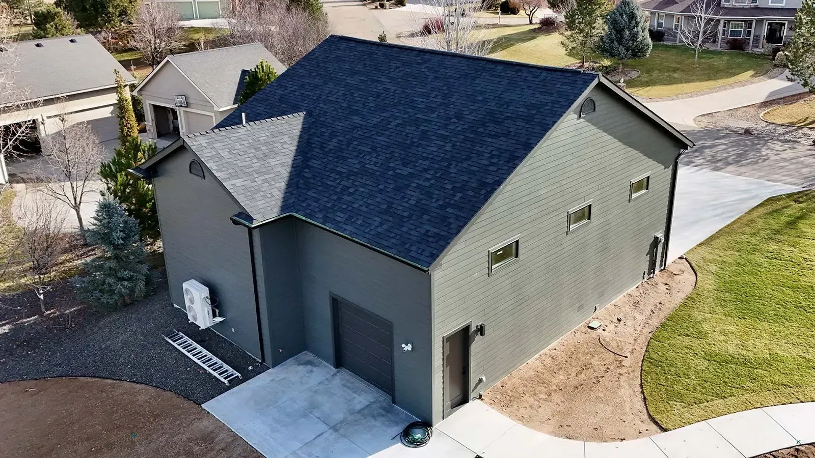 A two-story gray building with a dark blue roof, garage, and driveway in a suburban neighborhood.