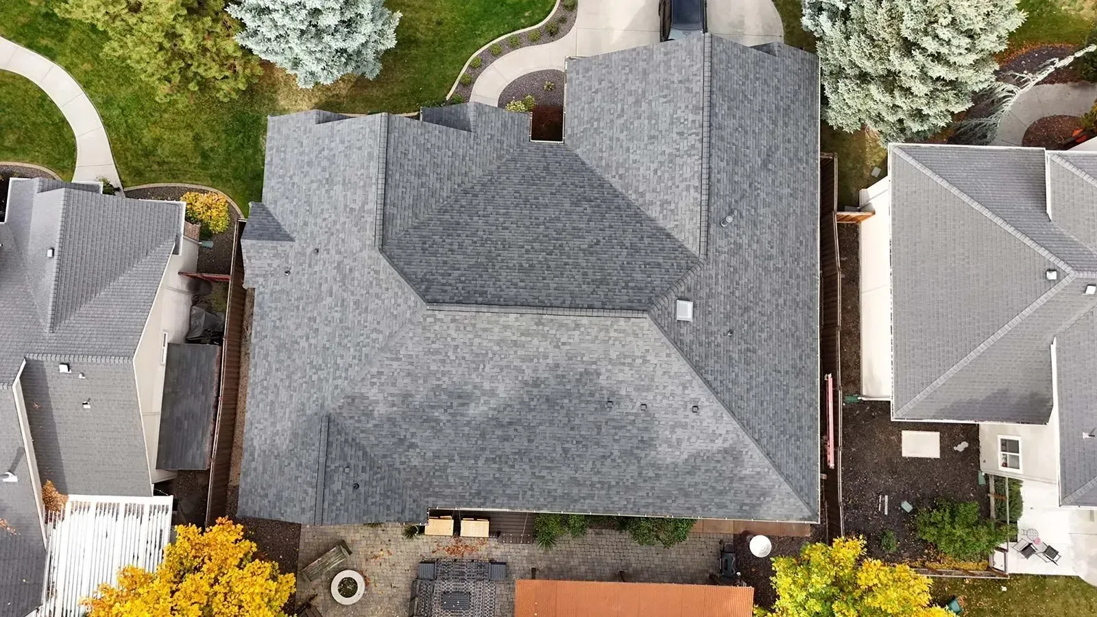 Overhead view of a gray asphalt shingle roof on a house, surrounded by other houses, trees, and landscaping.