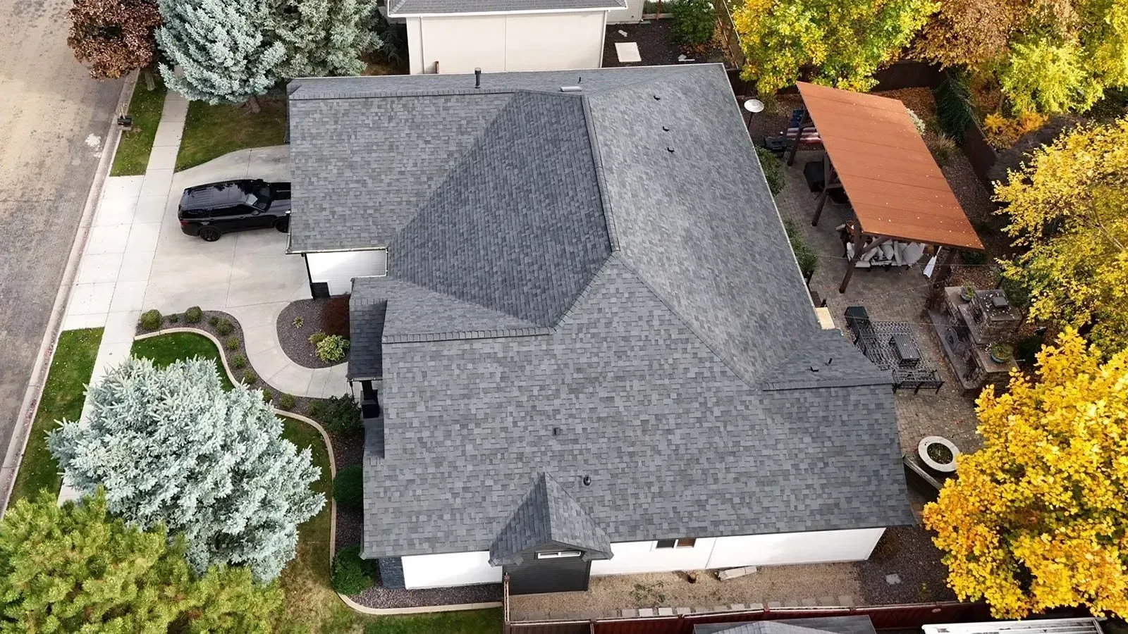Aerial view of a house with a dark gray roof, black car in the driveway, and a patio with an orange roof.