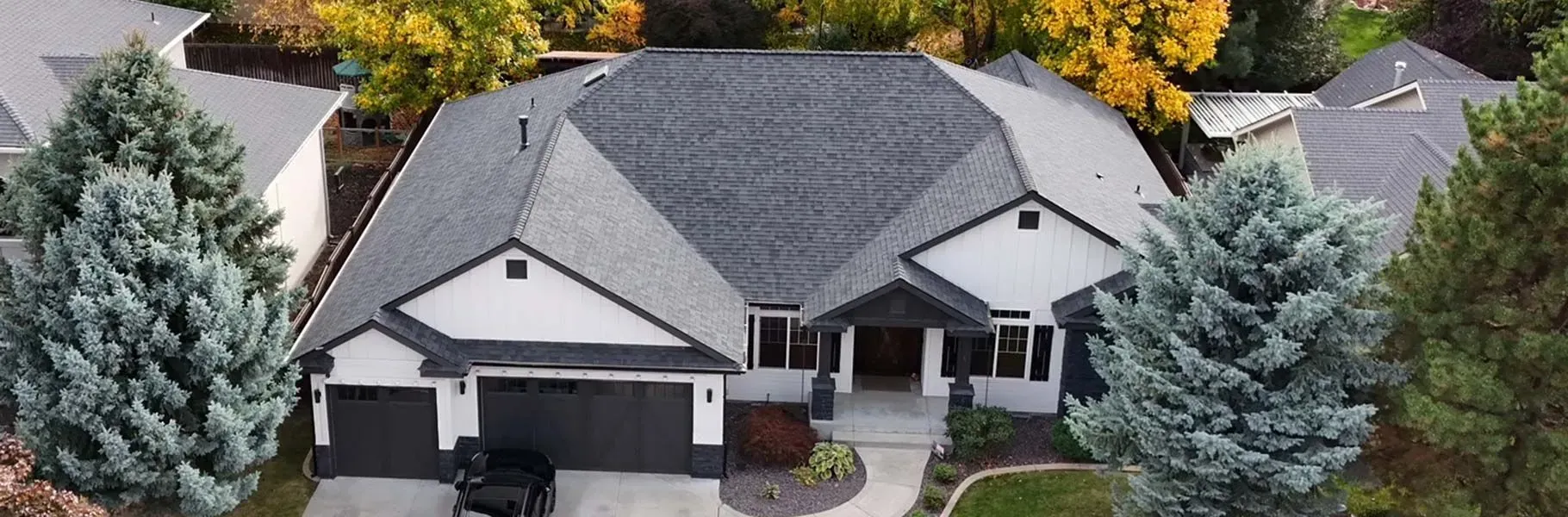 Aerial view of a modern house with a dark gray roof, white siding, and black trim, surrounded by trees.