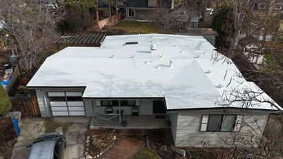 Overhead view of a one-story house with a white roof and garage door; bare trees surround it.
