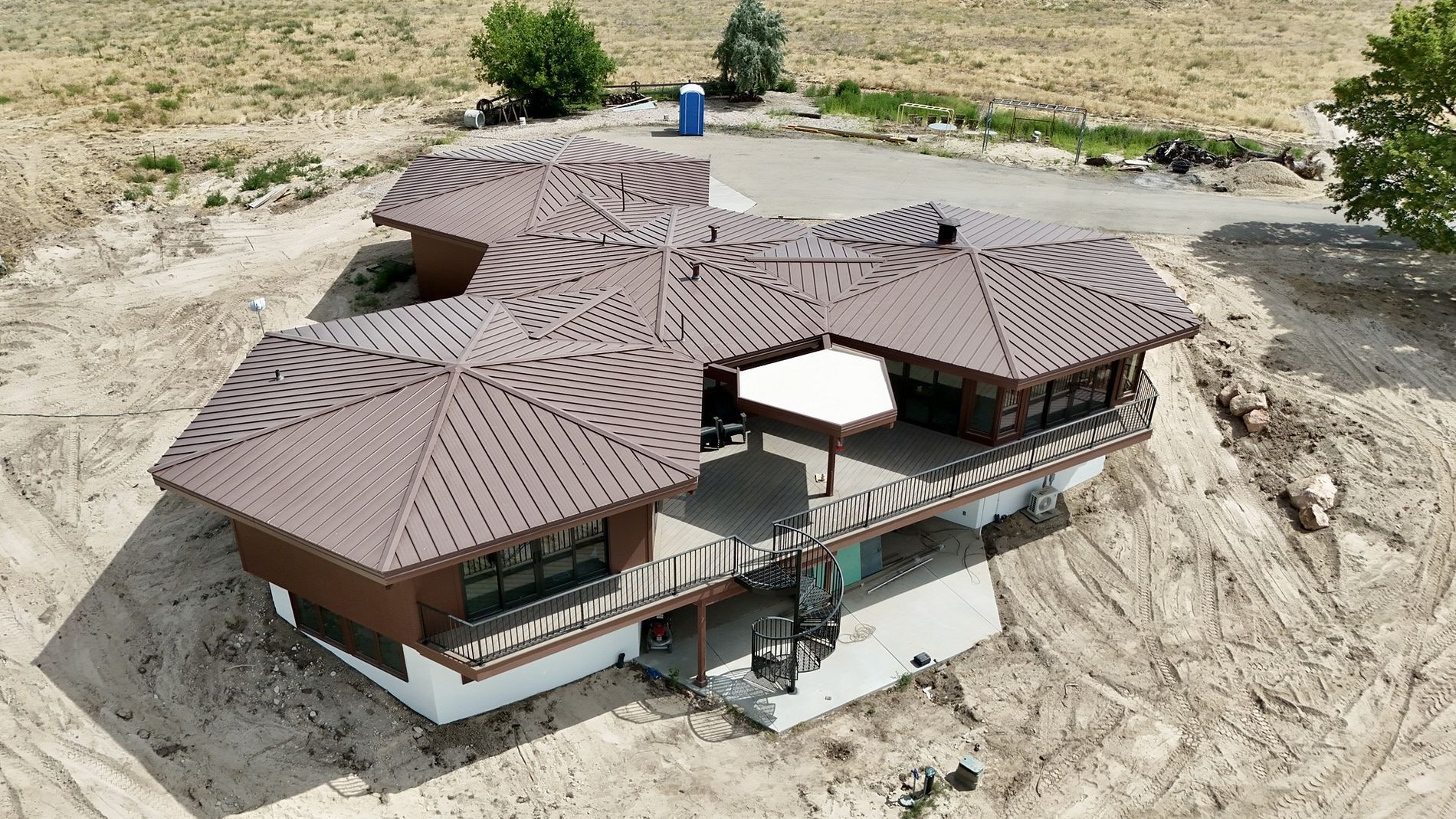 Brown-roofed, multi-section house on a hillside, surrounded by dirt and sparse vegetation.
