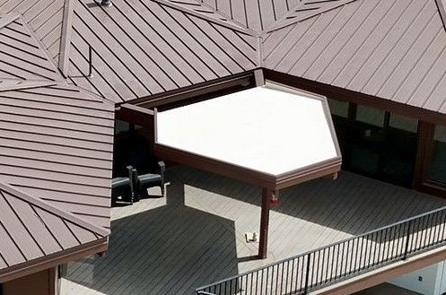 Brown metal roof, deck with awning, and black railing.