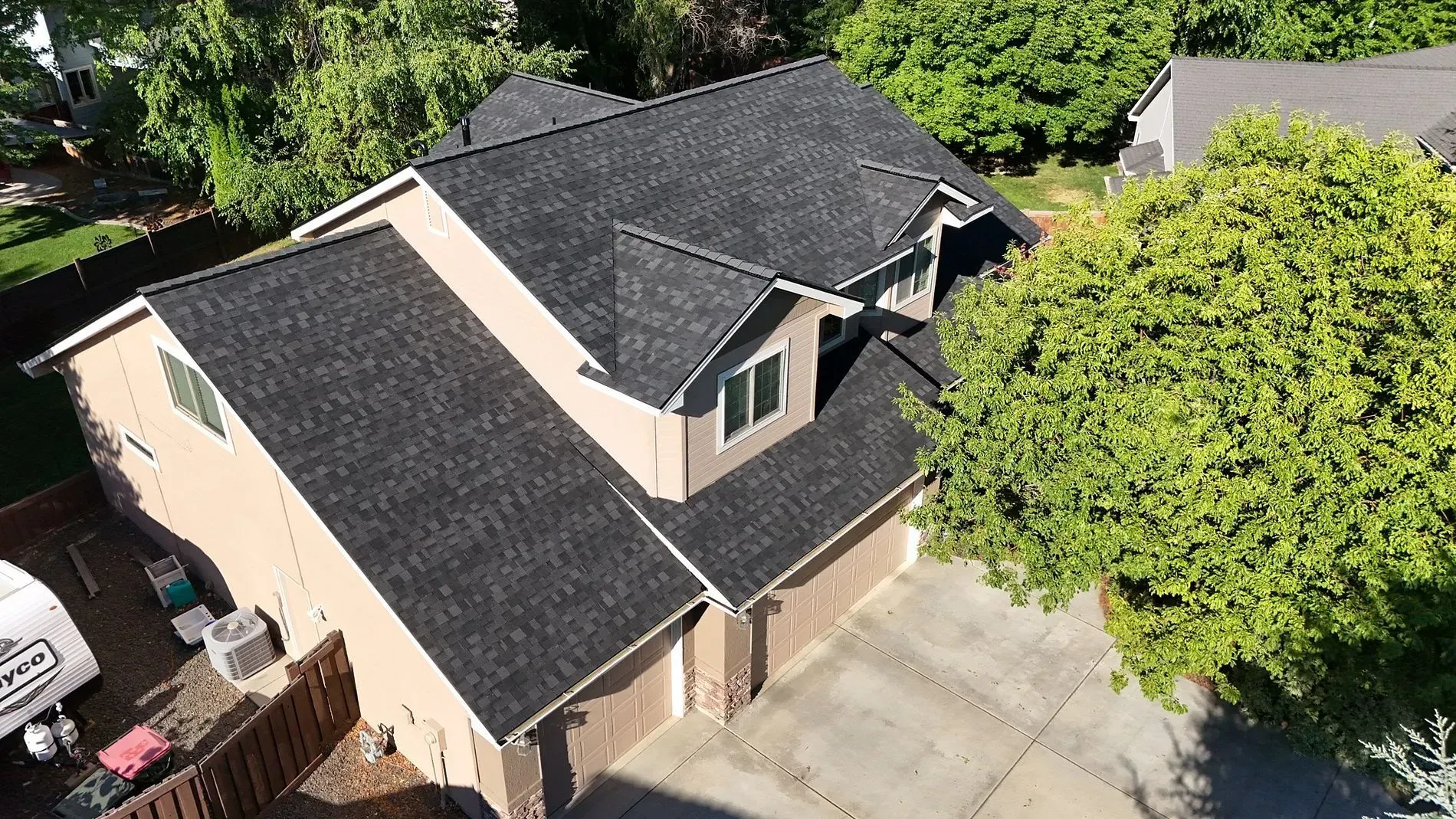Overhead view of a two-story house with dark gray roof, tan siding, and a large tree in the yard.