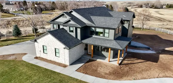 Modern two-story house with gray siding, white stone, and dark gray roof in a grassy area.