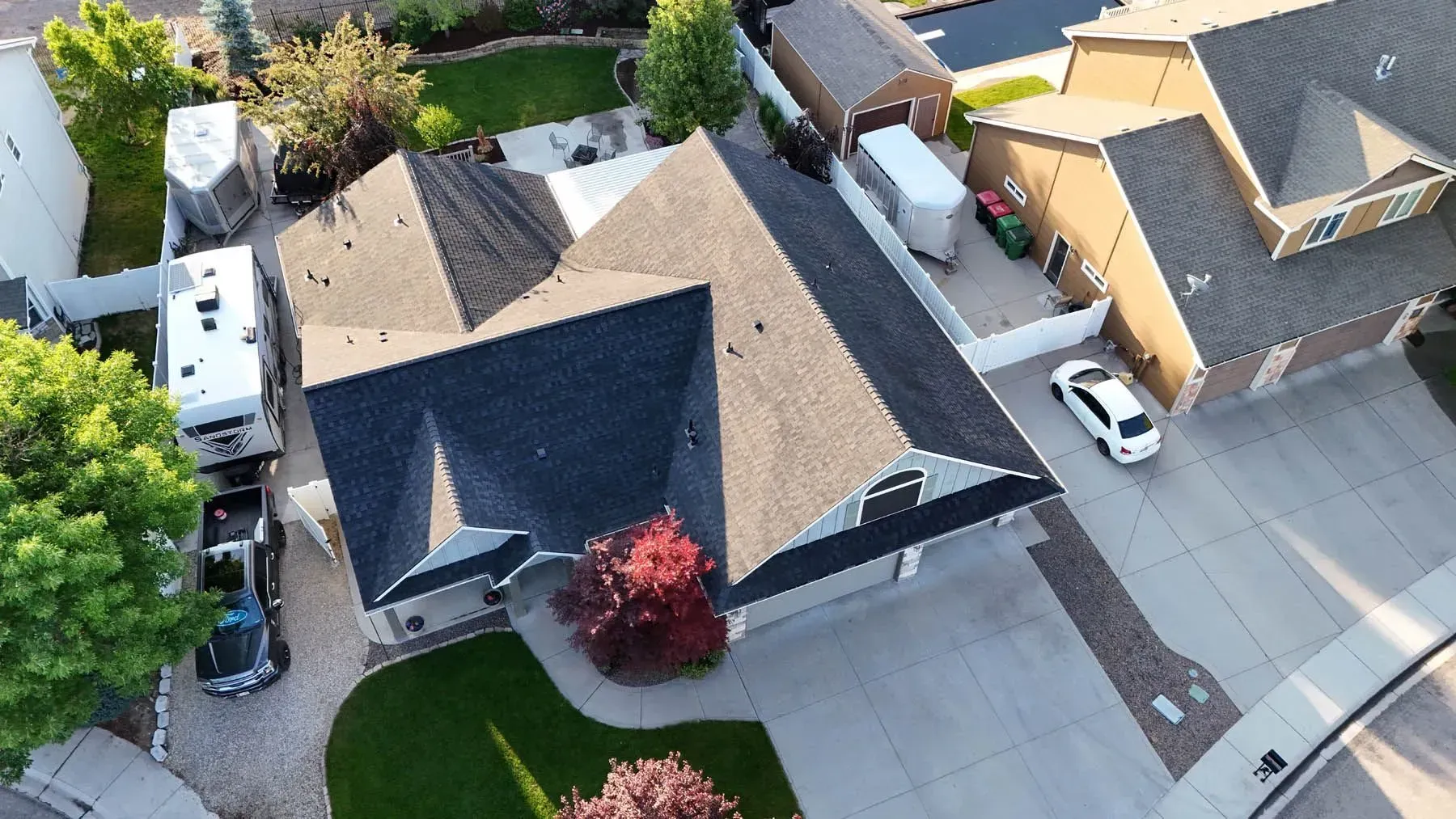 Aerial view of a suburban house with a dark roof and a driveway. A car and RV are parked nearby.
