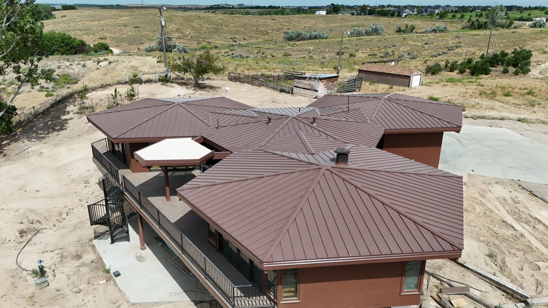 Brown metal roofed house with a deck overlooking a dry landscape under a blue sky.