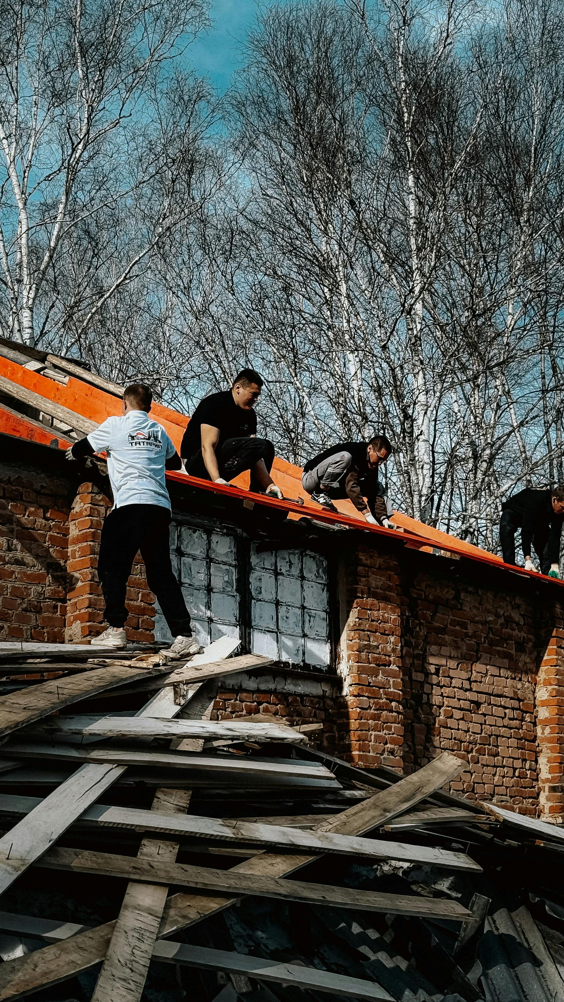 People standing on a damaged brick roof with debris below and trees in the background