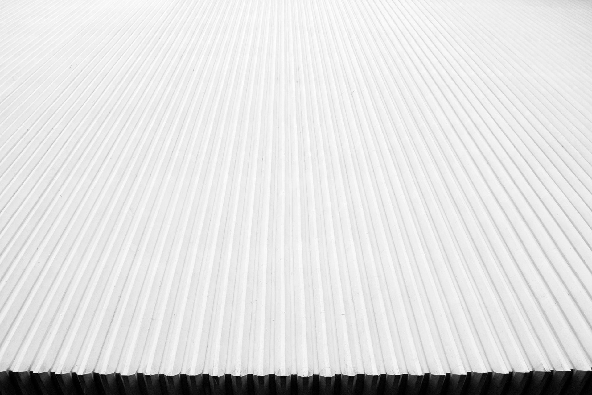 White, corrugated metal surface, viewed from a low angle, lines receding into the distance.