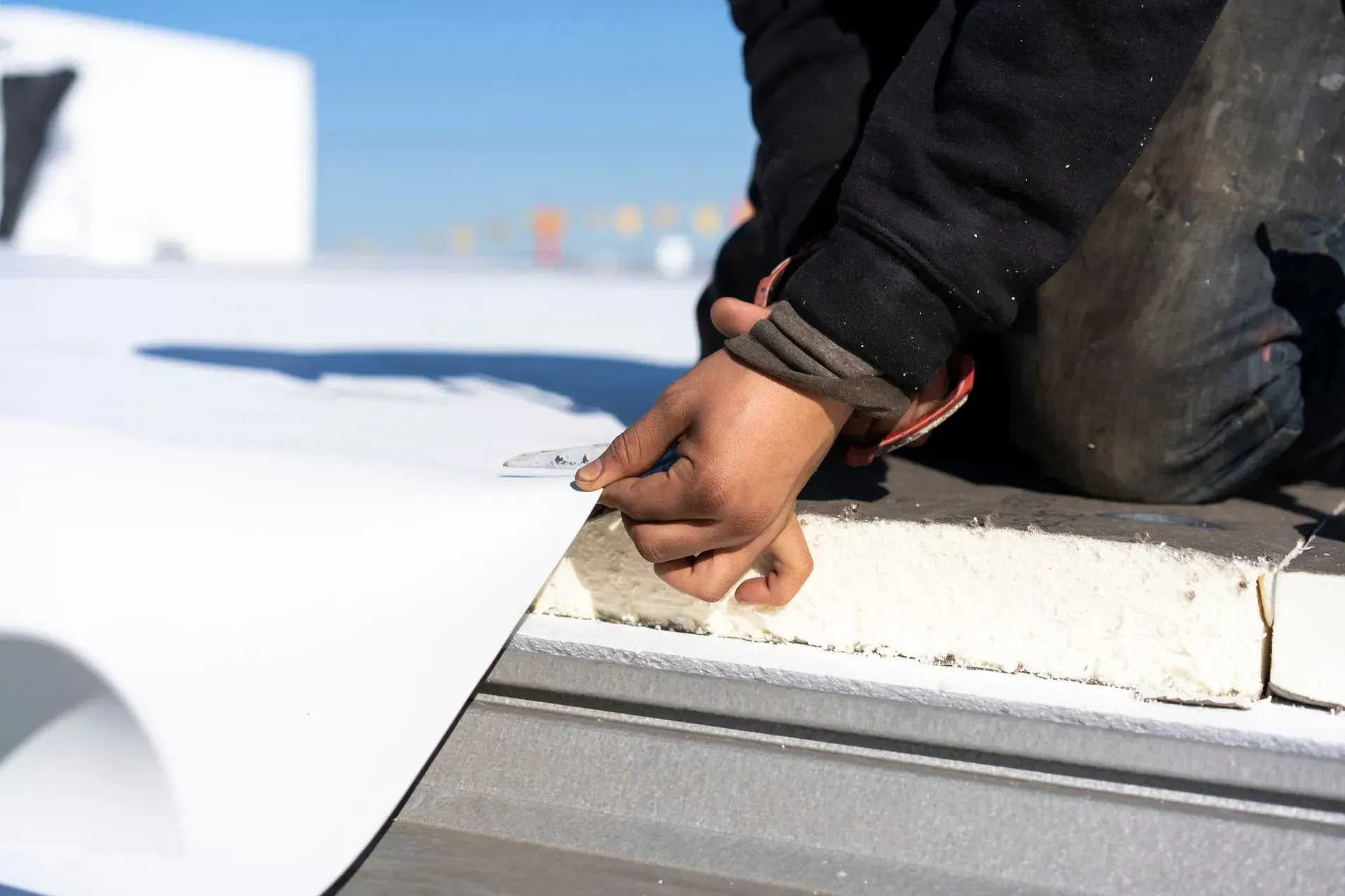 A person's hands pulling back the edge of white roofing material on a flat roof.