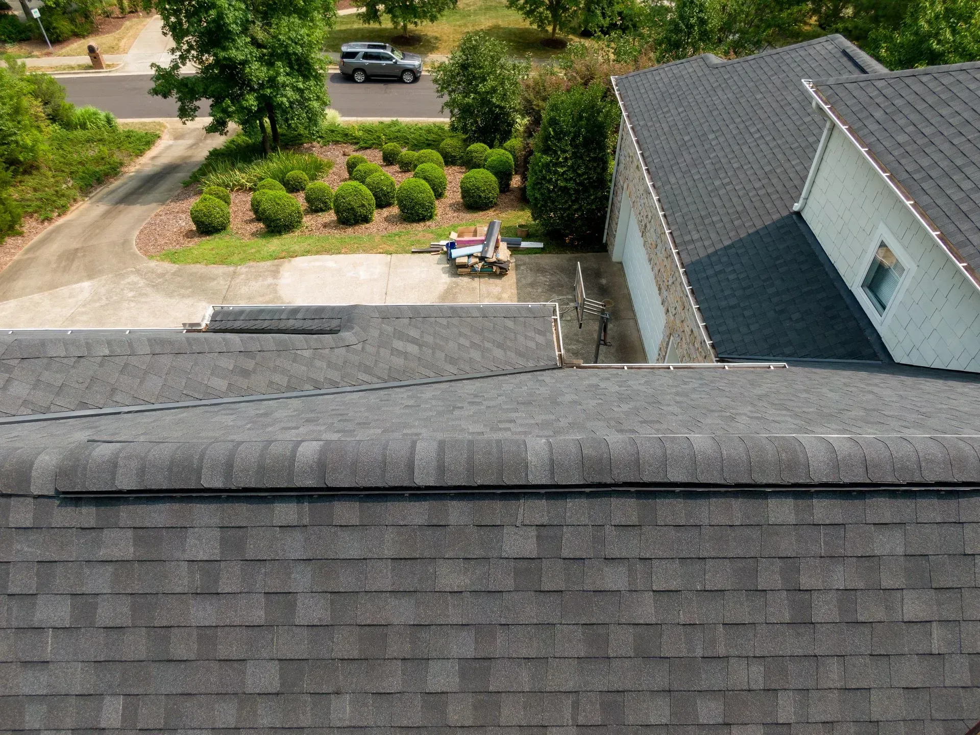 Aerial view of a modern house with a gray roof and black garage doors, flanked by blue-green trees.