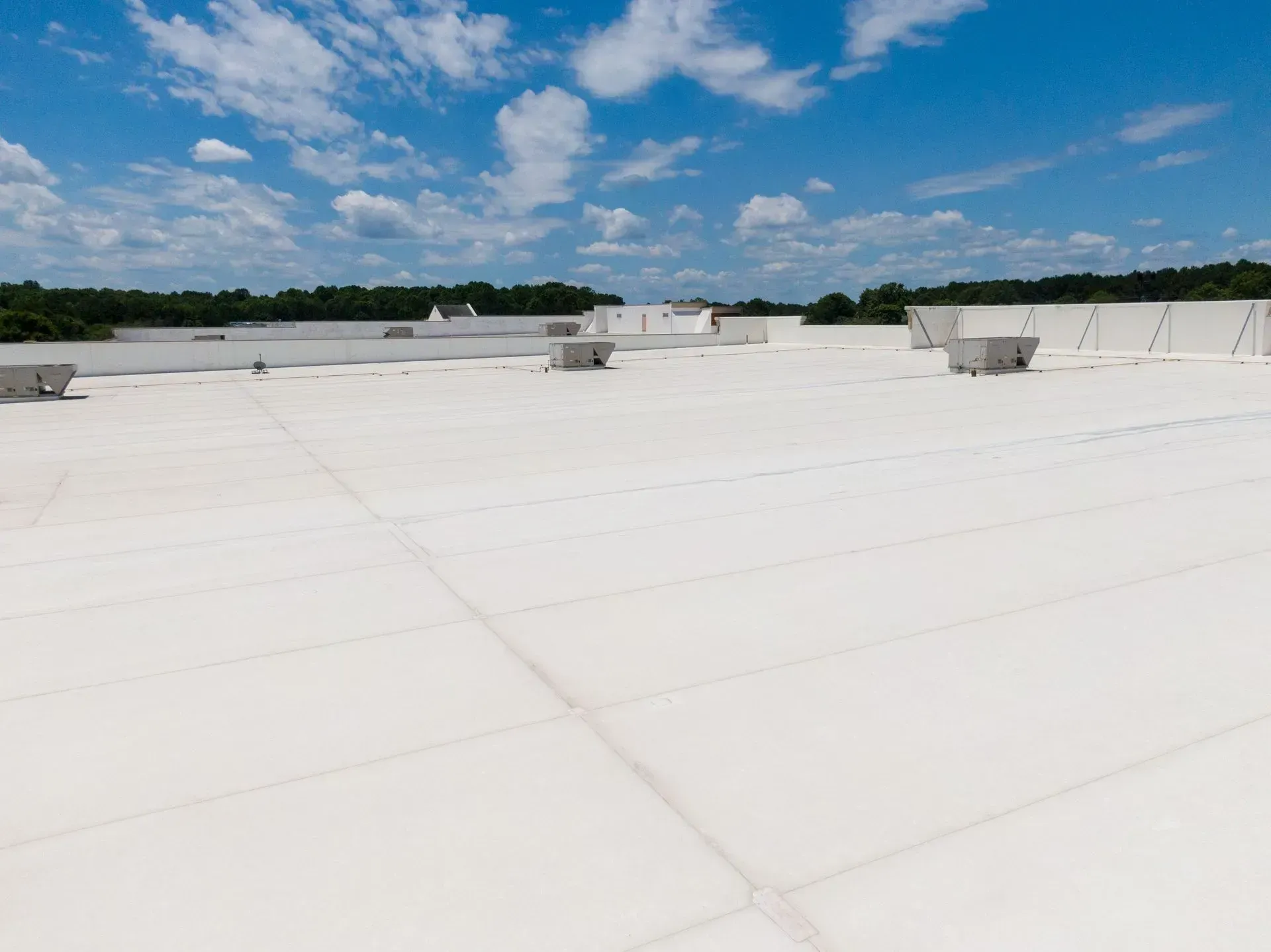 White commercial roof with mechanical units, blue sky, trees in the background.