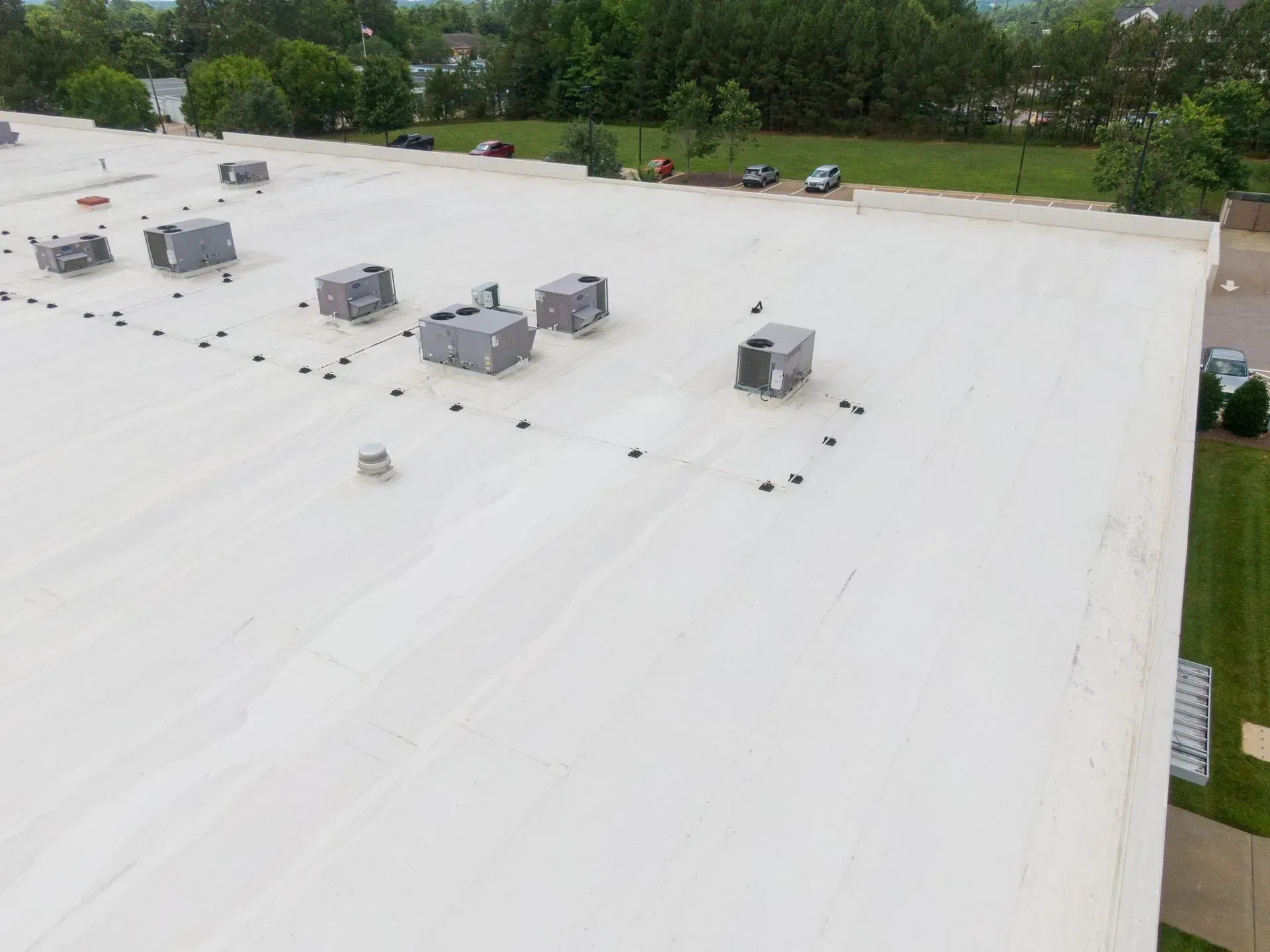 Aerial view of a white commercial roof with multiple HVAC units and scattered black objects.