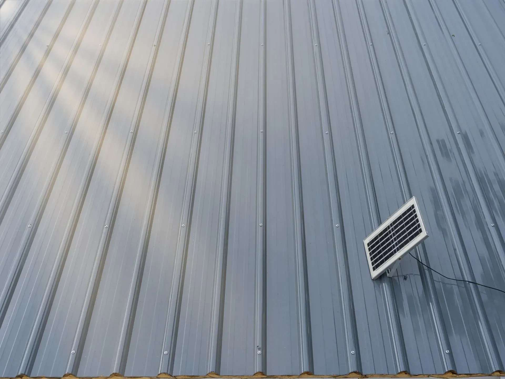 A small solar panel mounted on a gray, corrugated metal wall.