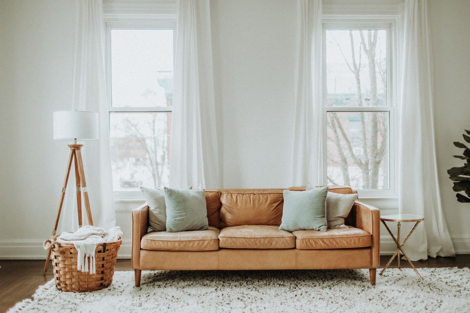 light brown leather couch in front of living room windows with a white textured rug underneath