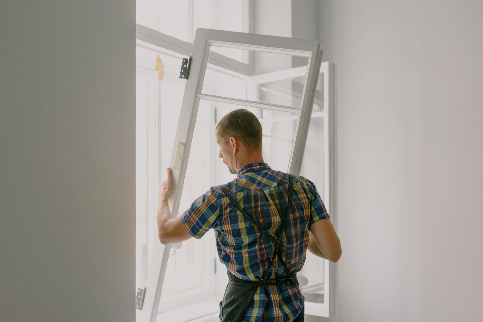 man placing a new window with white frame from inside a home
