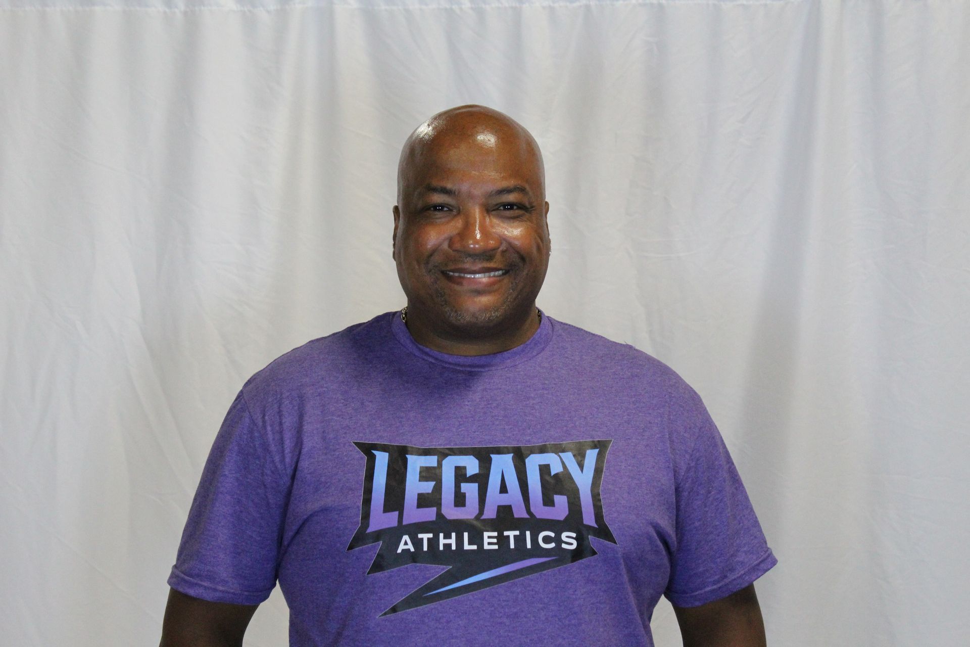 Man in blue t-shirt with logo, black pants, stands in an indoor setting.