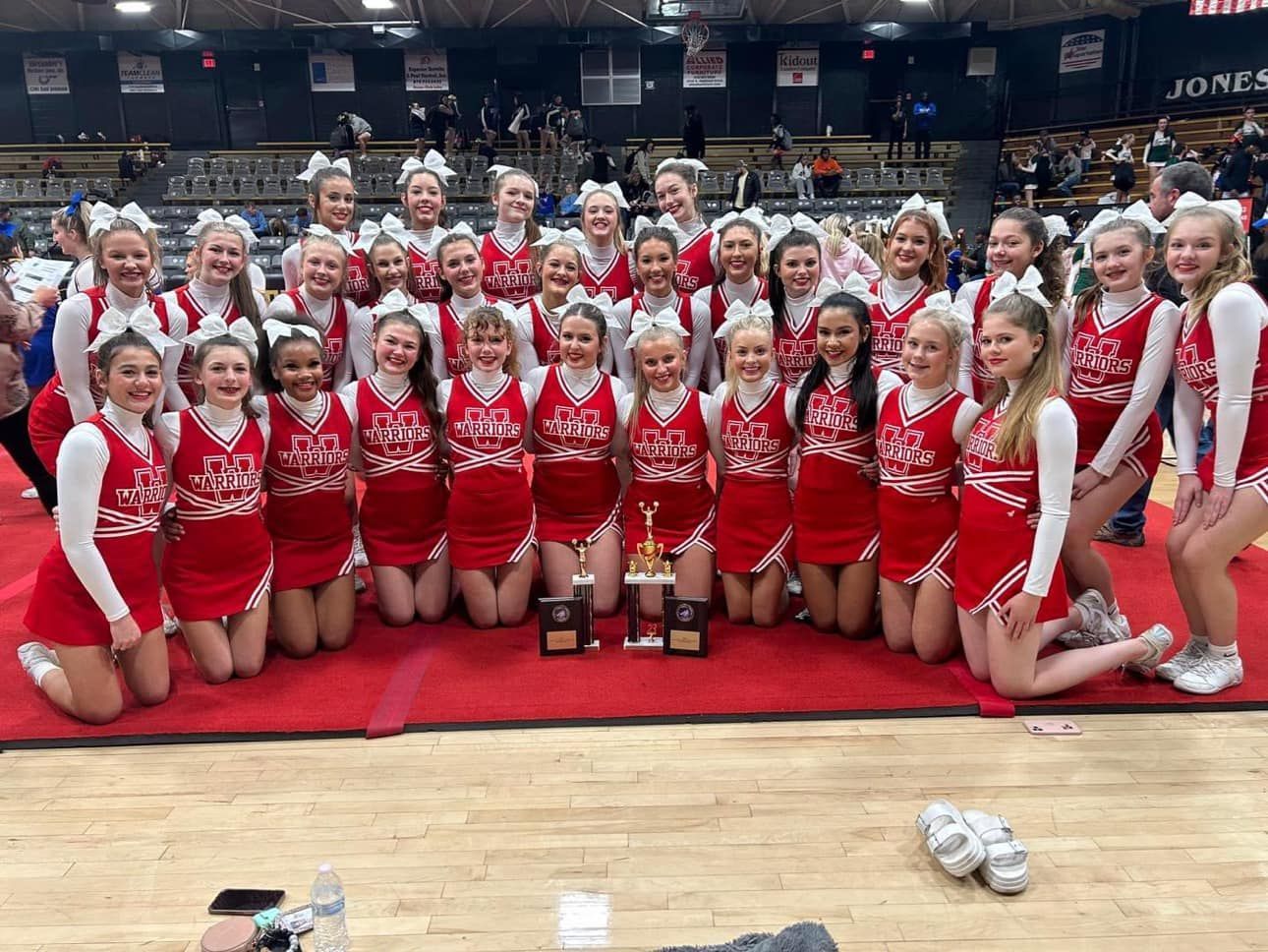 Three smiling girls standing on a blue mat, wearing athletic clothes in a gym.