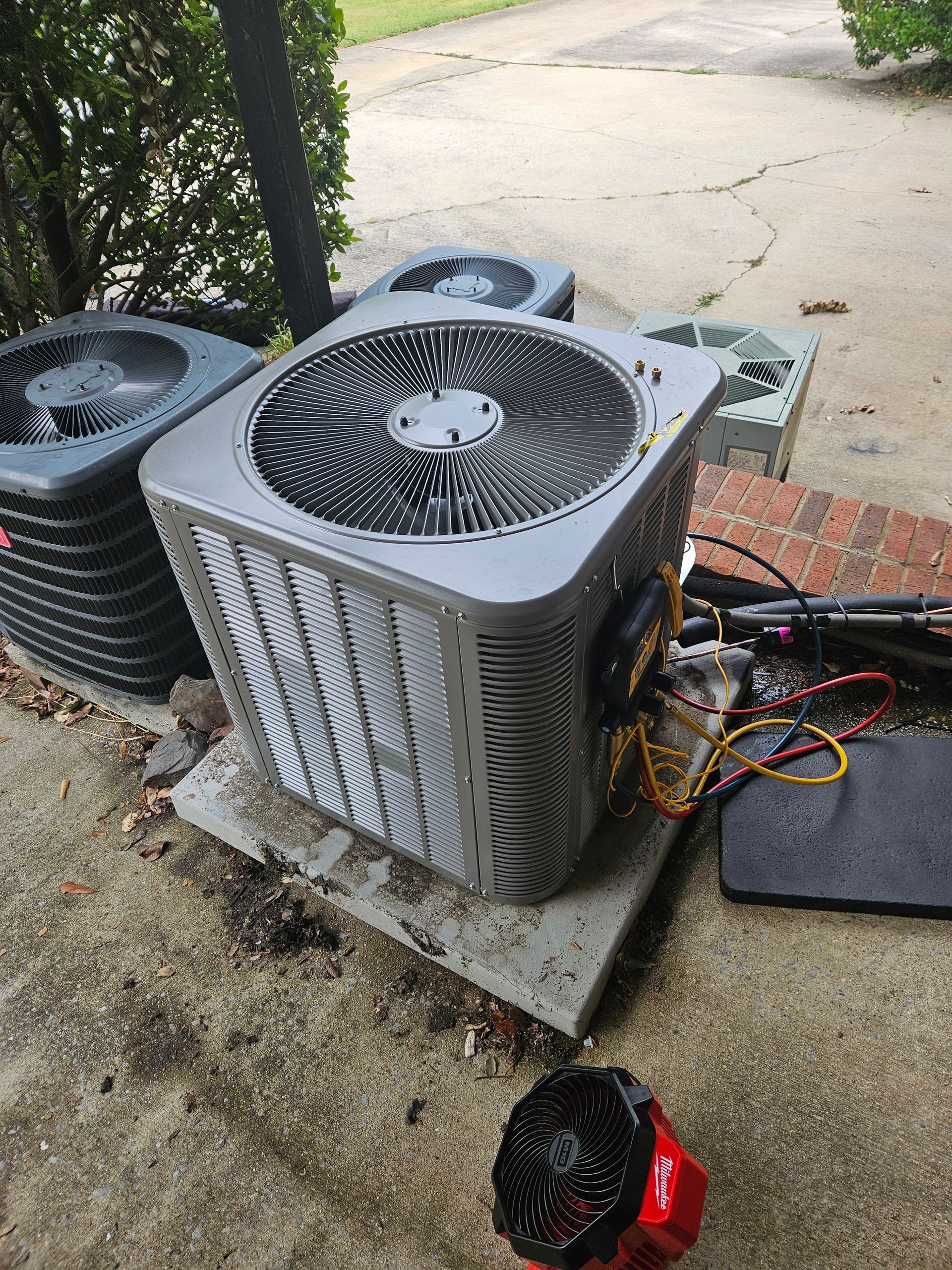An outdoor air conditioning unit sitting on a concrete pad. Other units and wires are nearby.
