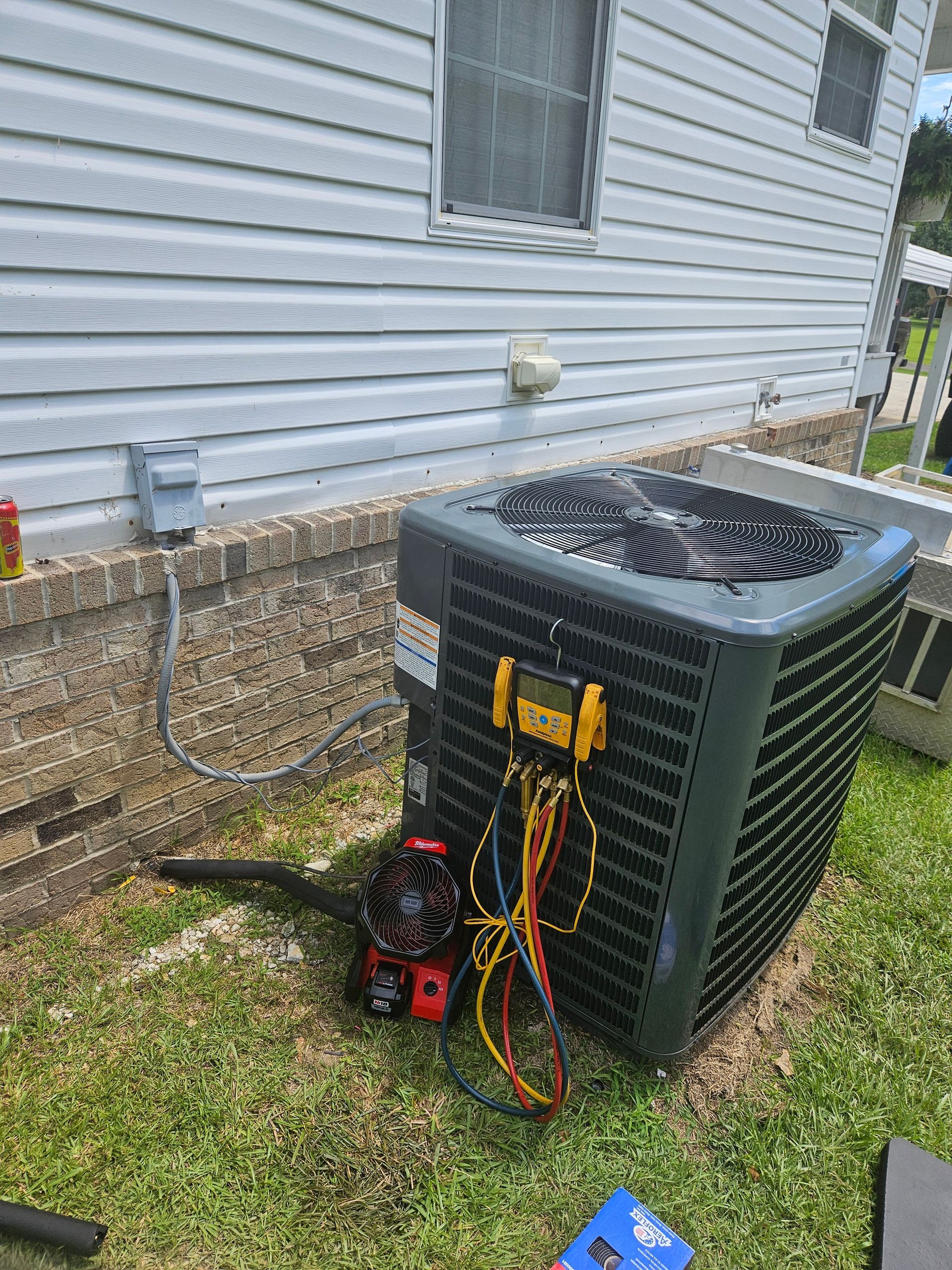 An air conditioning unit being serviced outdoors. A technician is using gauges and wires,