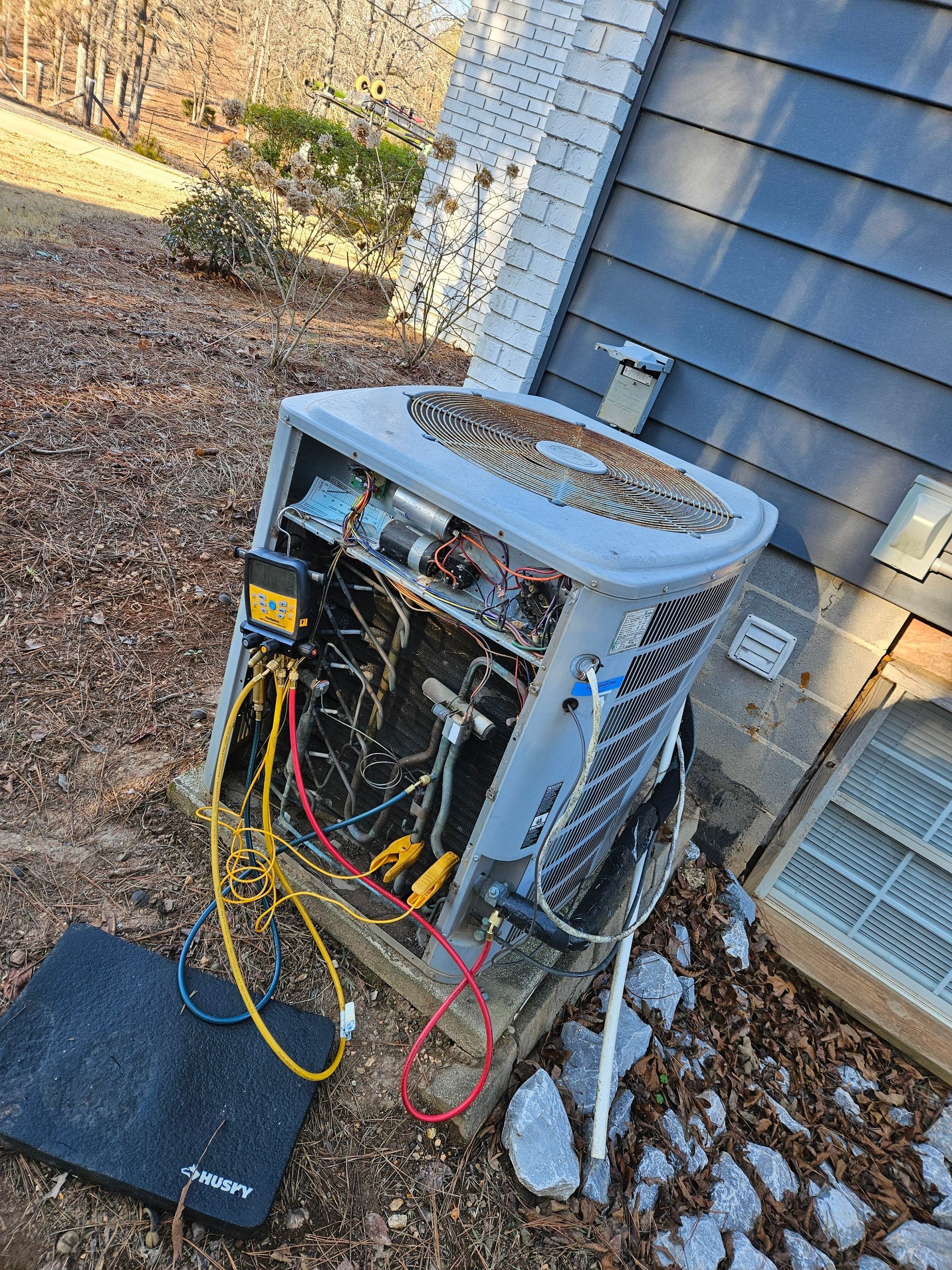 An open air conditioning unit being serviced outdoors, with wires and components visible.