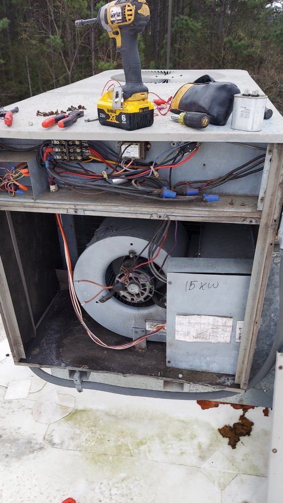 Open air conditioning unit on a roof, with exposed wiring and a fan. Tools lie on top, including a drill.