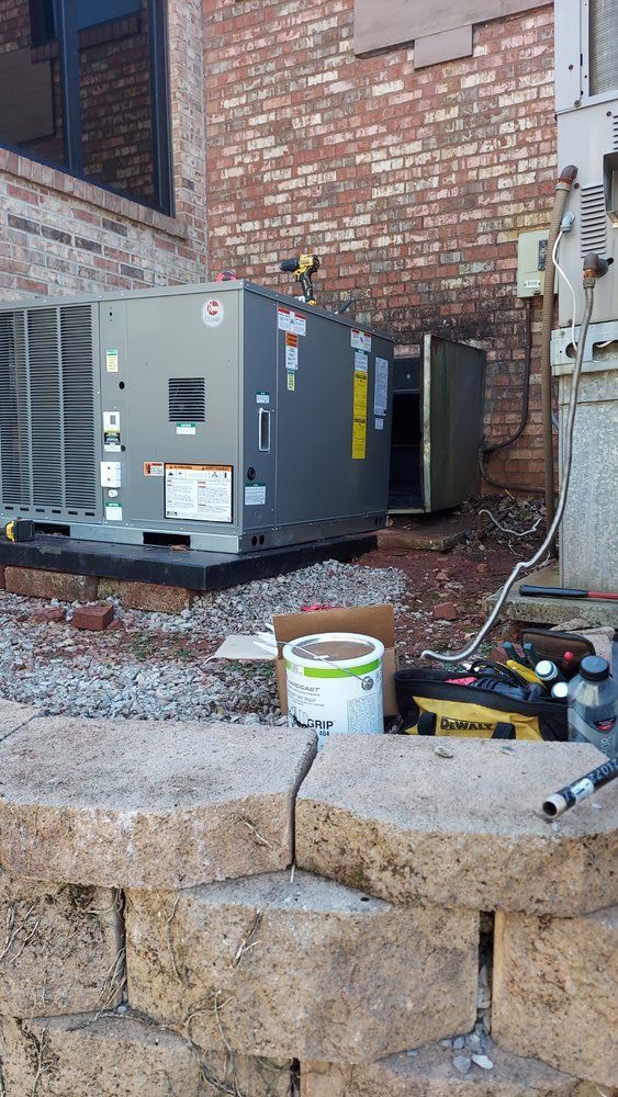 HVAC unit installation near a brick building. A new unit sits on a platform with tools and materials nearby.