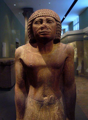 A statue of a man without a shirt is in a museum