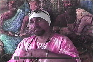 A man in a pink robe is sitting in front of a painting